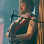 Músico cantando y tocando la guitarra durante un espectáculo típico escocés