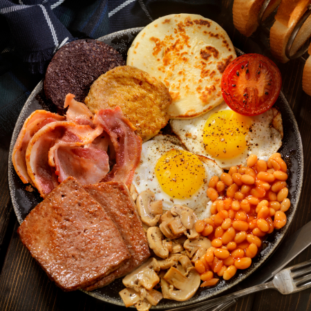 Desayuno tradicional escocés con haggis, pudding, salchichas, bacon, alubias, champiñones, tostada y tomate